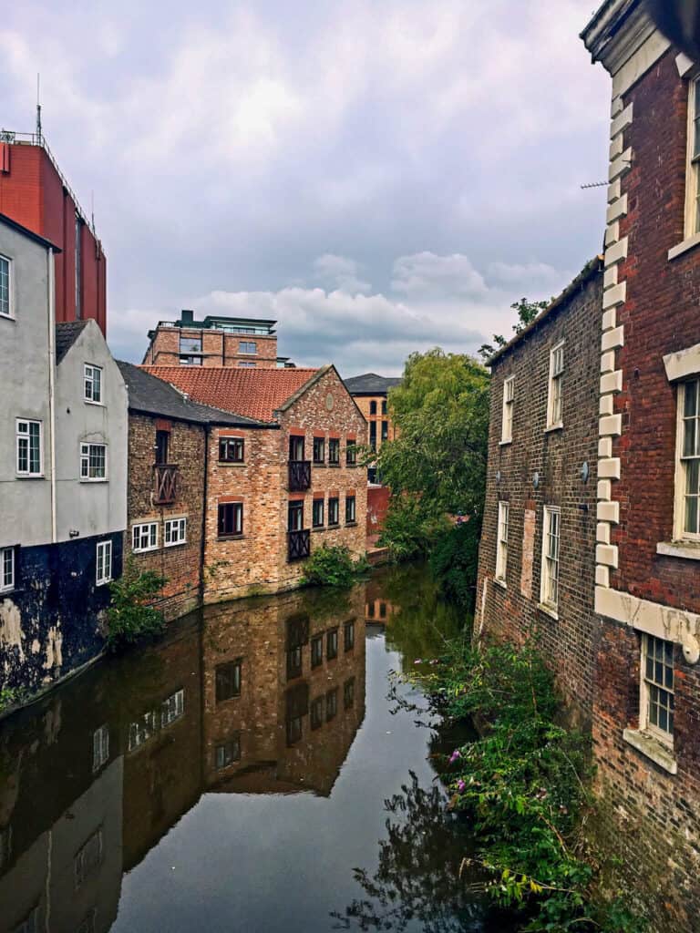 Historic York canal with old brick buildings and lush greenery.