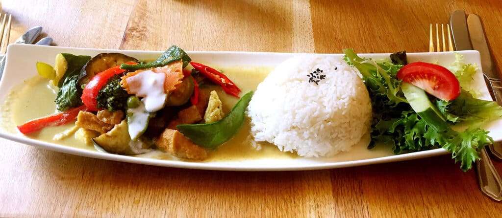 Tasty Asian chicken stir-fry with vegetables and rice on a long white plate.