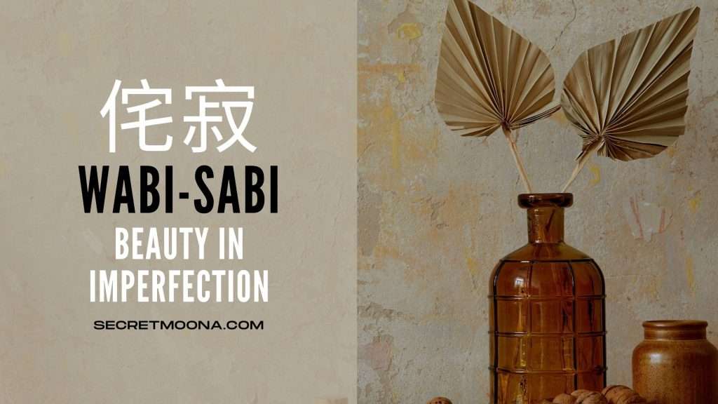 Wabi-sabi (侘寂) meaning beauty in imperfection, beside an amber glass bottle of dried palm fronds against a bare plaster wall