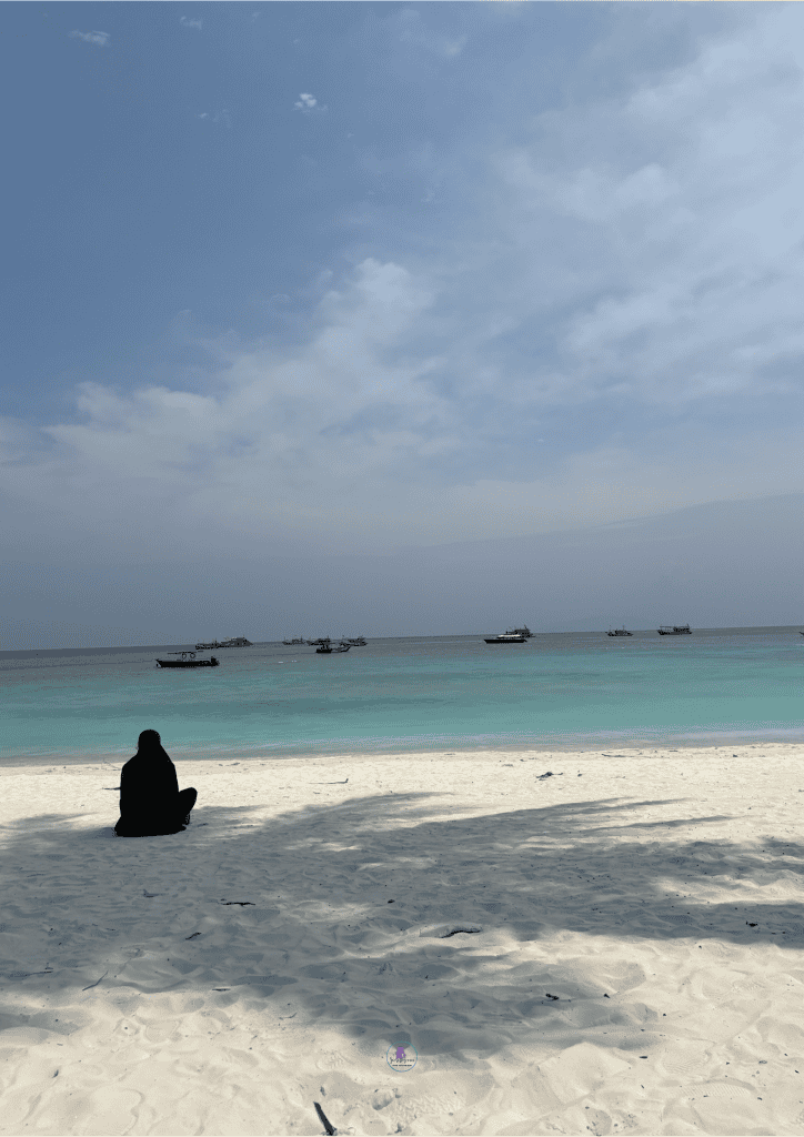 Woman in black sitting by the beach looking at the sea - Relaxation time Malaysia travel itinerary.