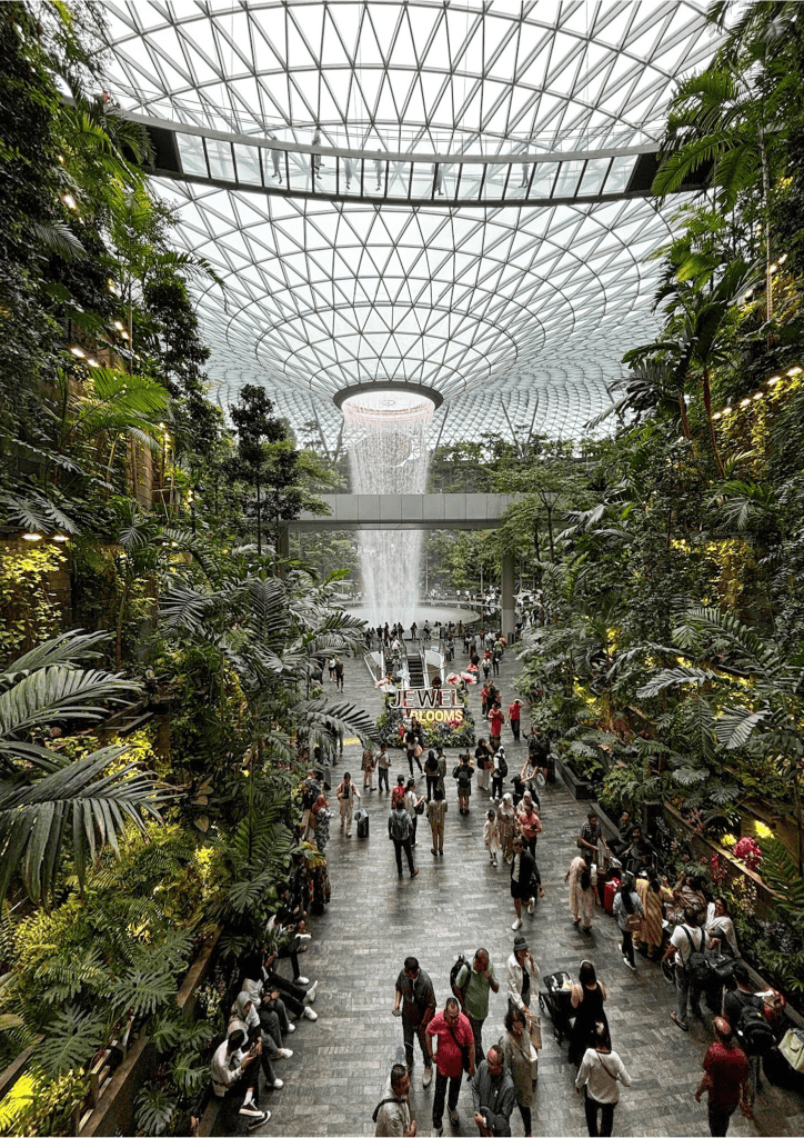 Indoor waterfall at Singapore Changi Airport surrounded by lush greenery and numerous visitors. 