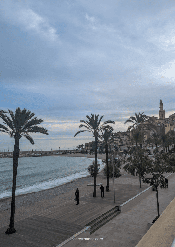 The Perfect One Day in Menton Itinerary: Discover Hidden Gems 22 A picturesque balcony view showcasing a beach and swaying palm trees - One day in Menton