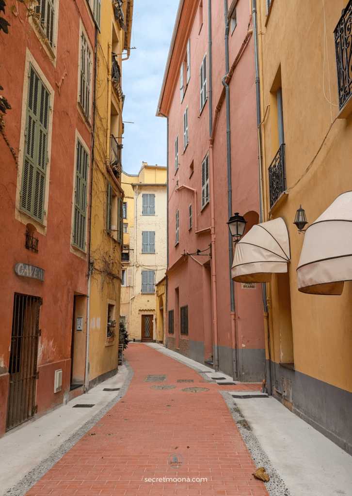 The Perfect One Day in Menton Itinerary: Discover Hidden Gems 4 A narrow street in Menton featuring a red brick wall and a white umbrella