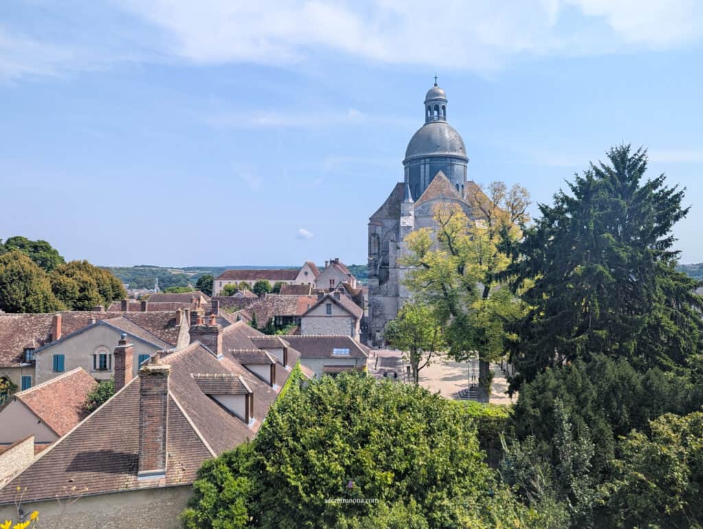 Church steeple over rooftops in a charming European village, lush green trees, sunny weather, picturesque scenery.