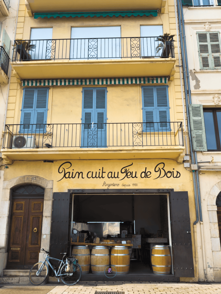 Traditional bakery in Cannes with the sign “Pain cuit au feu de bois” and blue shutters above the storefront.