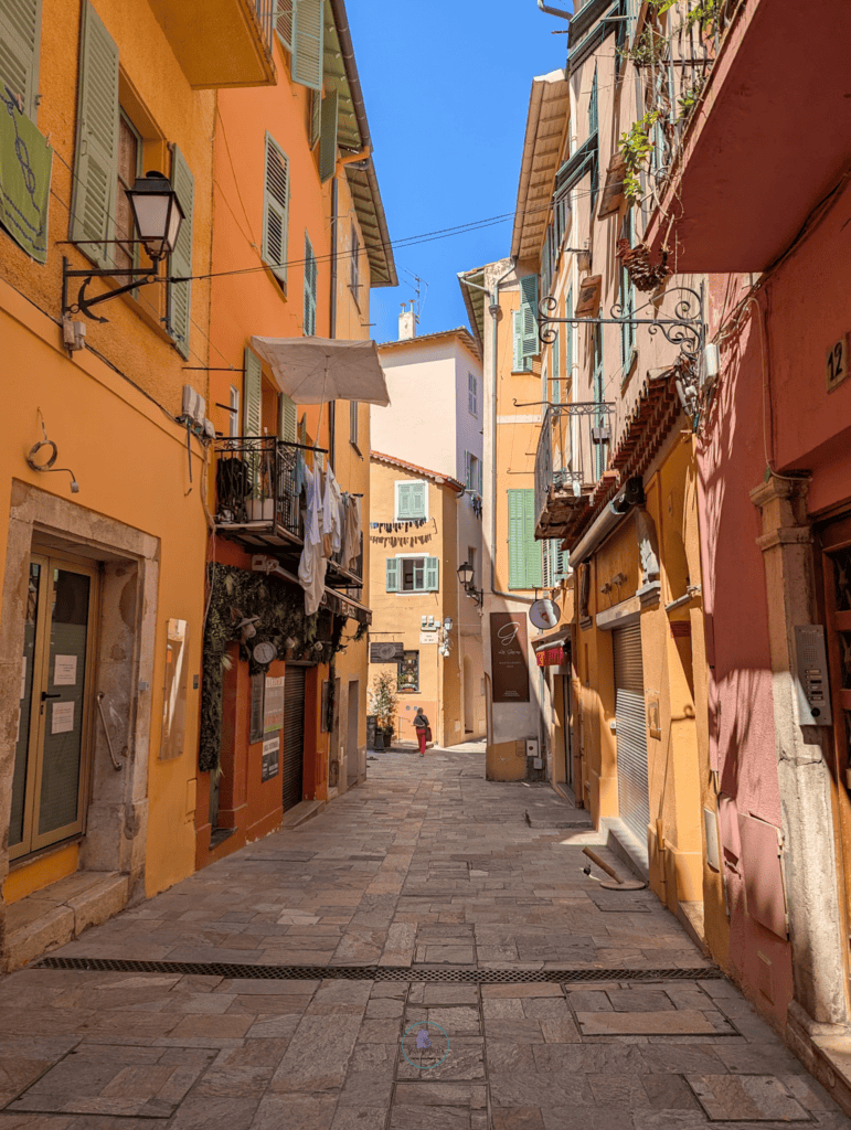 How To Spend One Day In Villefranche-sur-Mer: Things To Do 8 Narrow old town street in Villefranche-sur-Mer with pastel buildings and shutters