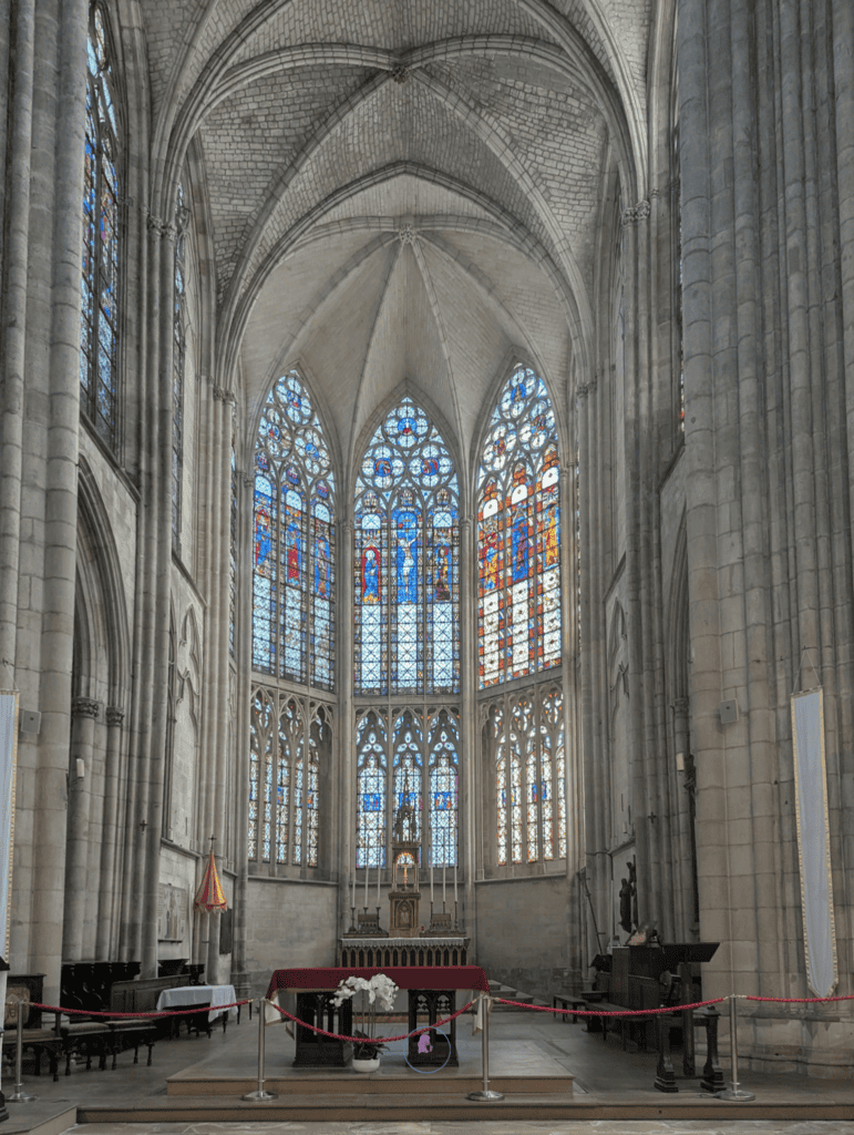 Tall Gothic cathedral interior in Troyes with stained glass windows above the altar