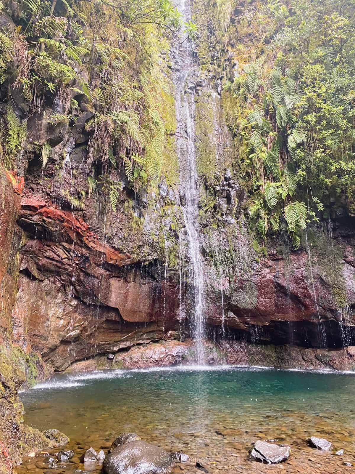 A tall waterfall dropping into a green pool in a rock amphitheatre at 25 Fontes, Rabaçal