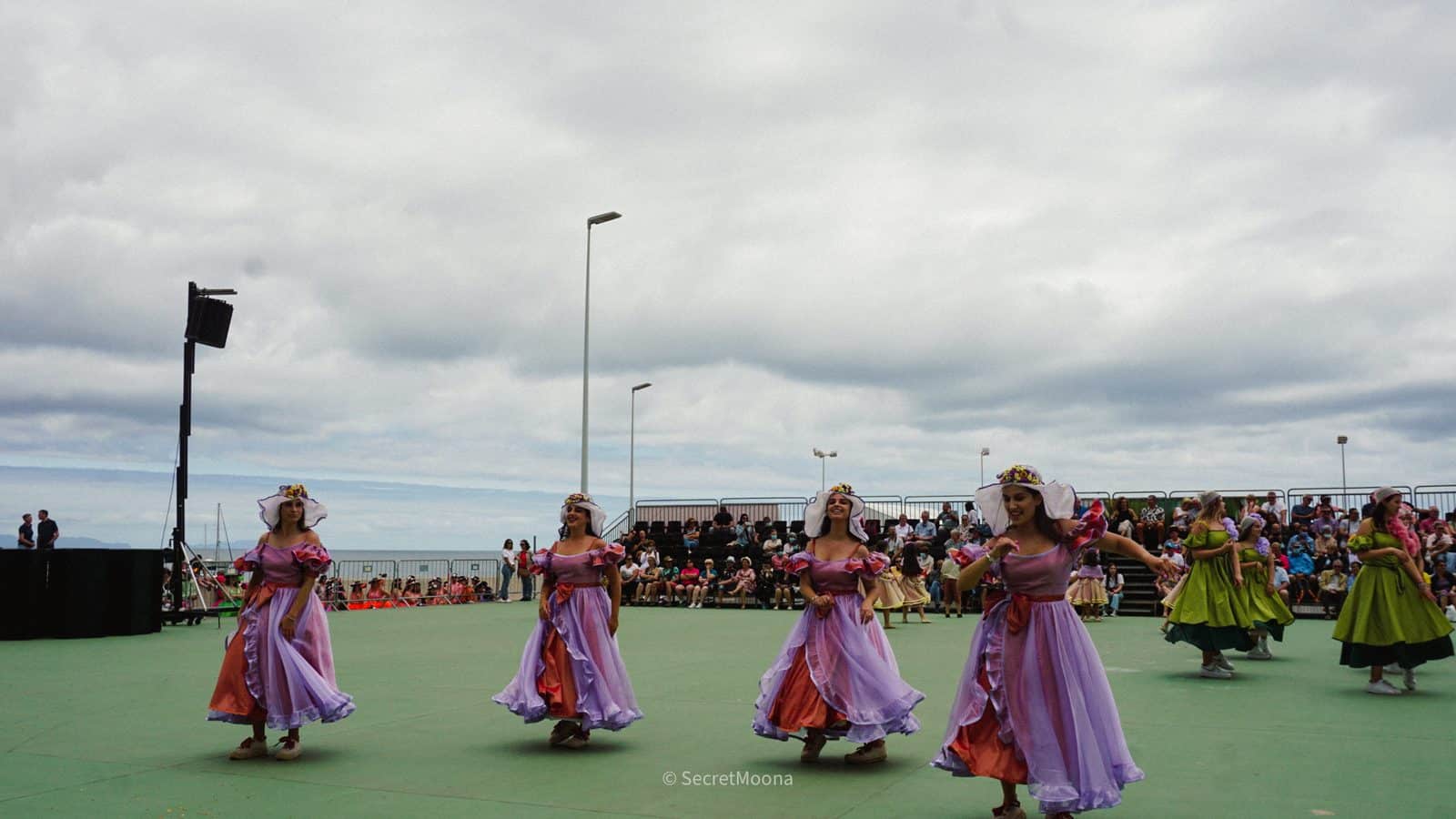 Folk dancers in pink and lilac traditional dresses performing outdoors during the Madeira flower festival