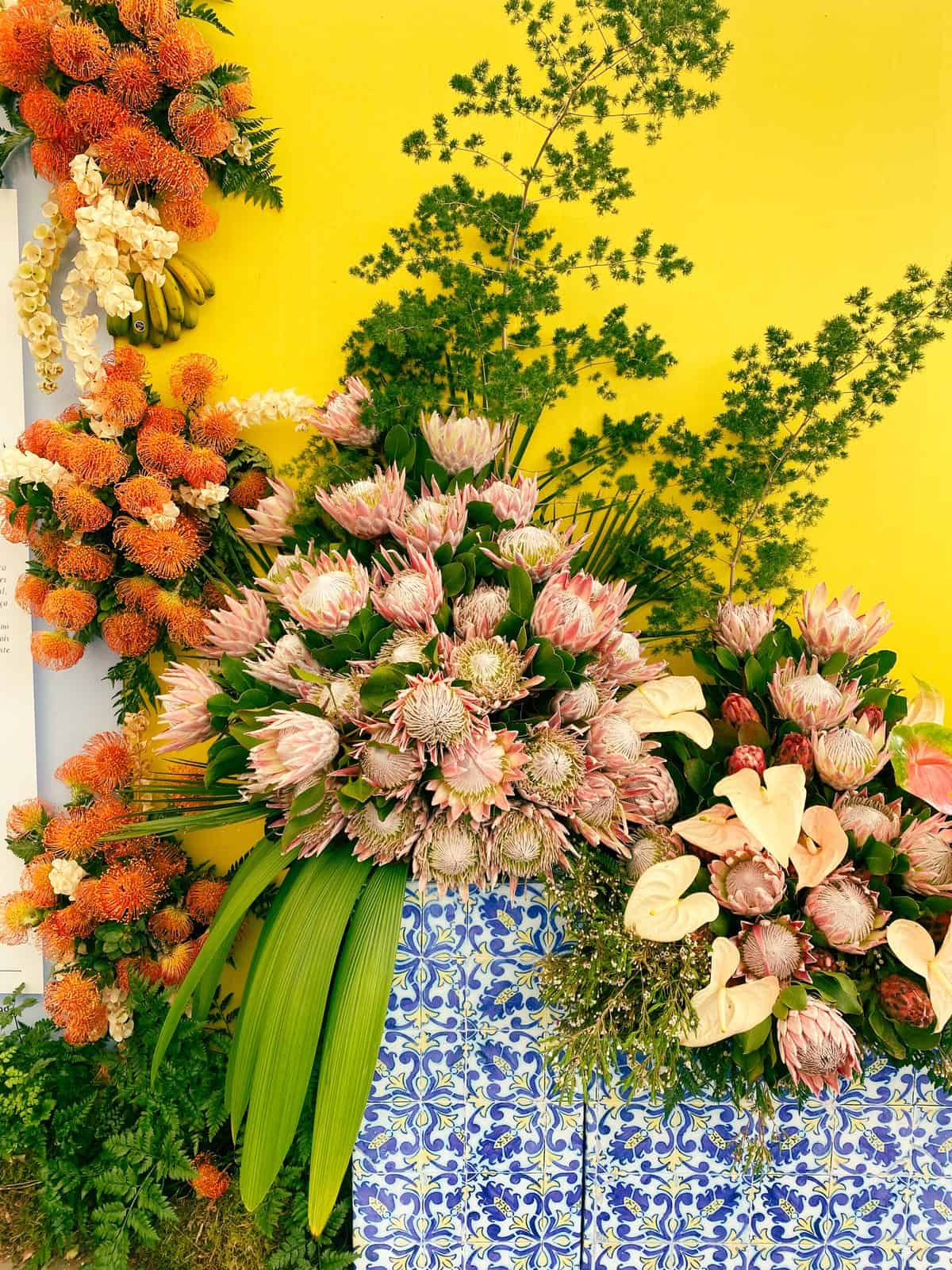 A tall arrangement of proteas and tropical flowers set against a blue-and-white azulejo panel