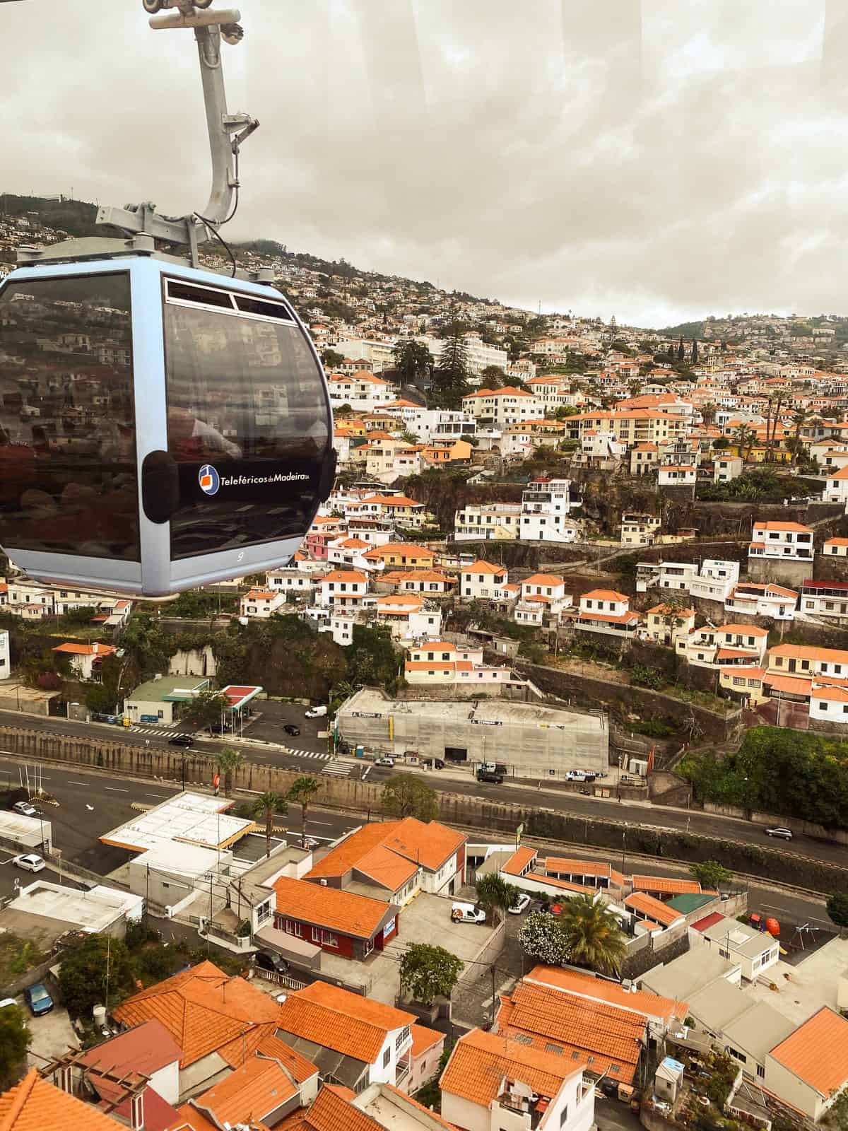A cable car cabin climbing above the orange rooftops of Funchal towards Monte