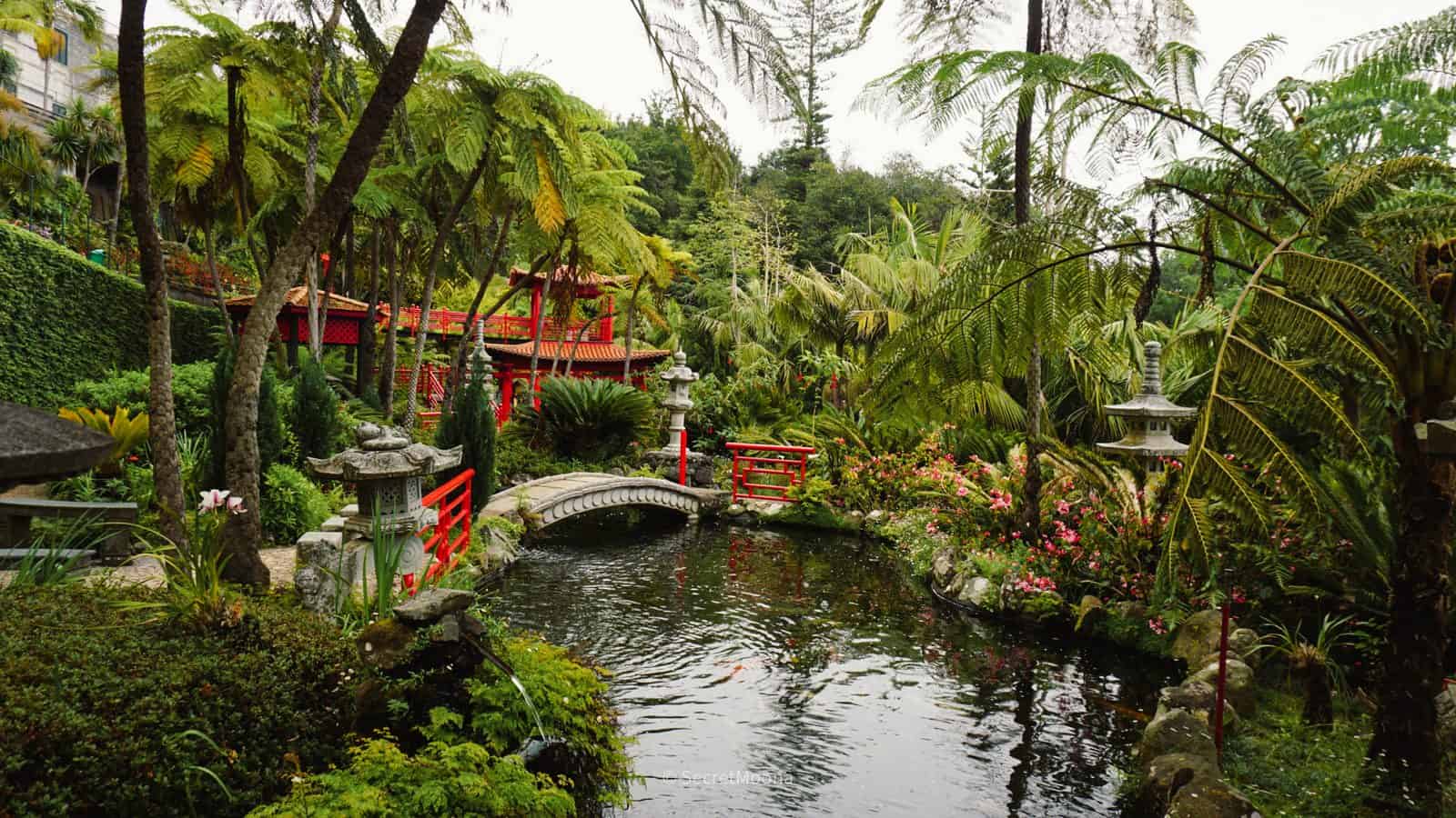 A red pagoda and arched bridge reflected in a koi pond in the oriental garden at Monte Palace