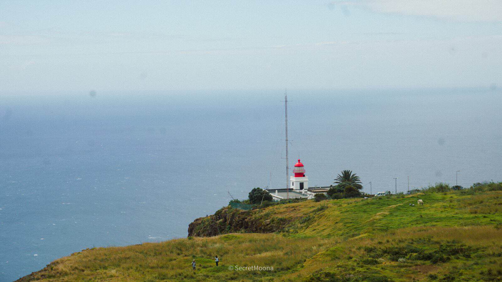 The red-and-white striped lighthouse at Ponta do Pargo on a grassy clifftop above the Atlantic