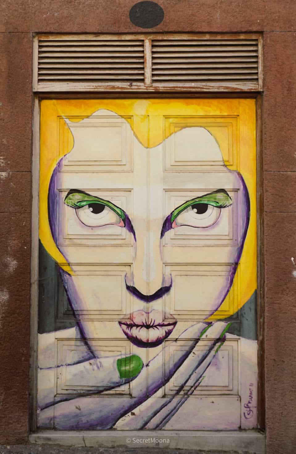 A painted door on Rua de Santa Maria in Funchal's Old Town showing a stylised face in yellow and purple