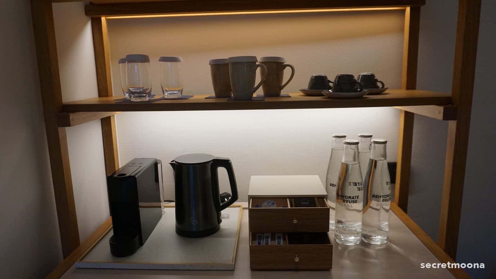 Kettle, glasses, mugs and a timber tea chest on a lit shelf in a room at Hilton Burau Bay Langkawi