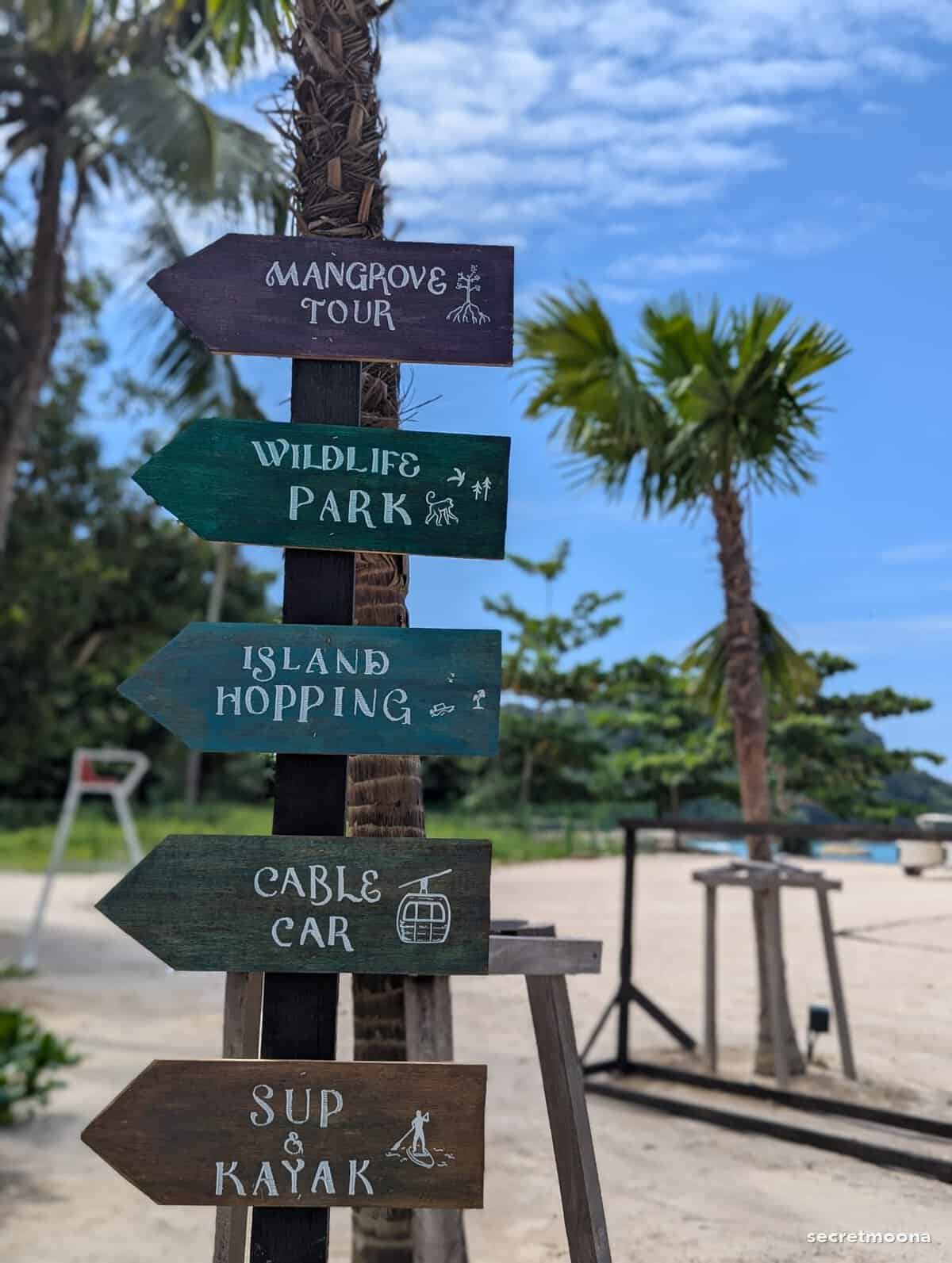 A wooden signpost pointing to the mangrove tour, wildlife park, island hopping and cable car
