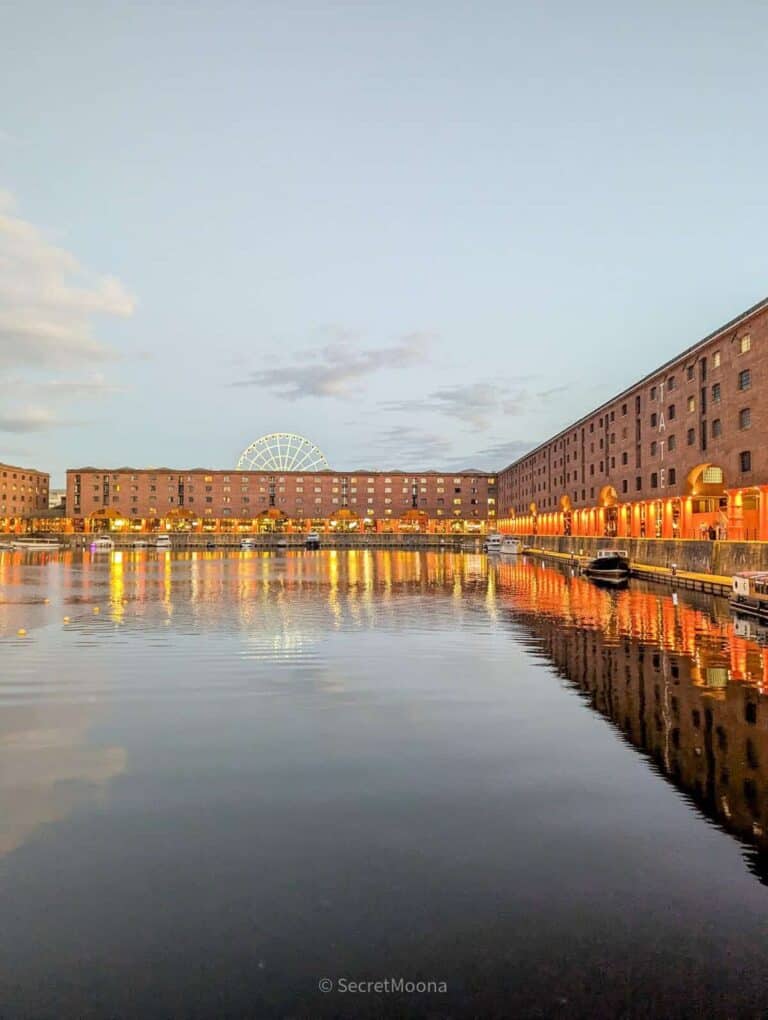 Royal Albert Dock warehouses lit orange at dusk, reflected in the dock water